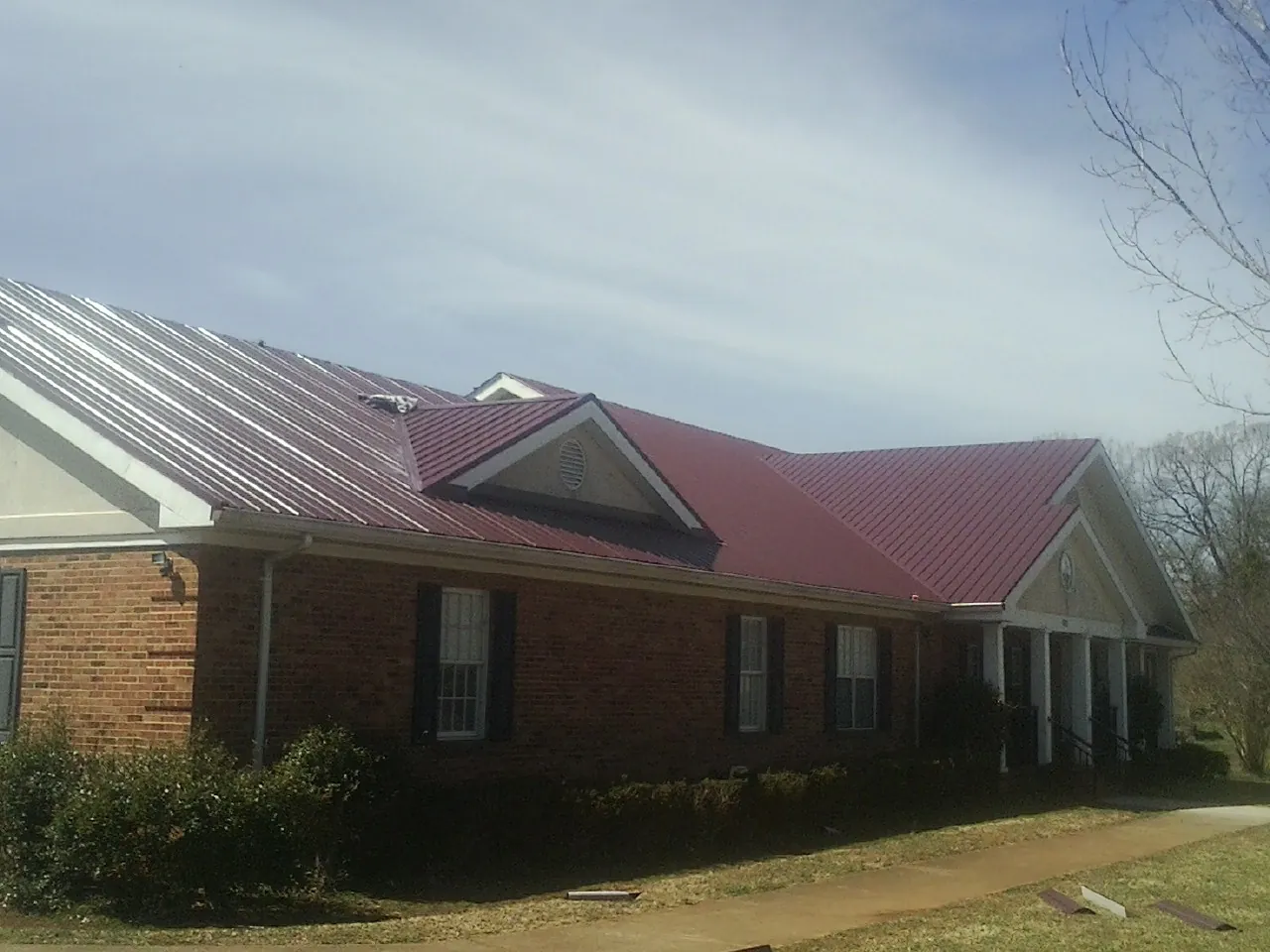 Red metal roof with gabled entries on a long brick building, from a Hail Damage Roof Repair job in Saluda